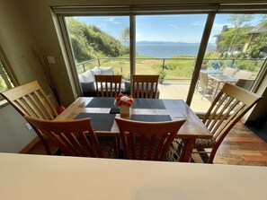 A dining area with a table and chairs, a vase of flowers, and a view of a balcony with outdoor furniture and a scenic landscape.