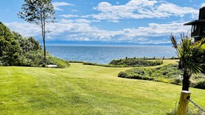 A well-maintained grassy area with a view of the ocean and a clear sky. - Points West Oceanfront Resort 3 bedroom Ocean Point Beach House  (Sooke)
