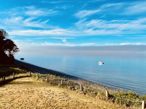 A beach with a fence, a boat, and calm water under a clear sky.