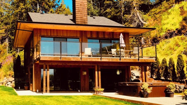 A modern two-story house with large windows, a balcony, and a well-maintained garden. - Points West Oceanfront Resort 3 bedroom Ocean Point Beach House  (Sooke)