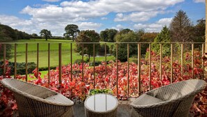 A balcony with wicker chairs and a view of a green field and trees. - Colleton Hall - Six Bedroom Villa, Sleeps 12 (Rackenford)