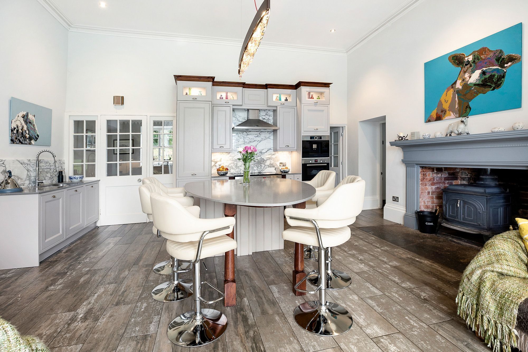 Een moderne keuken met witte kasten, een marmeren spatwand en een ronde eettafel met witte stoelen.