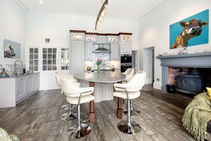 A modern kitchen with white cabinetry, a marble backsplash, and a round dining table with white chairs.