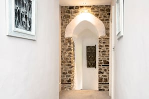 A hallway with a stone wall, an arched doorway, and a framed picture on the wall. - Colleton Hall - Six Bedroom Villa, Sleeps 12 (Rackenford)