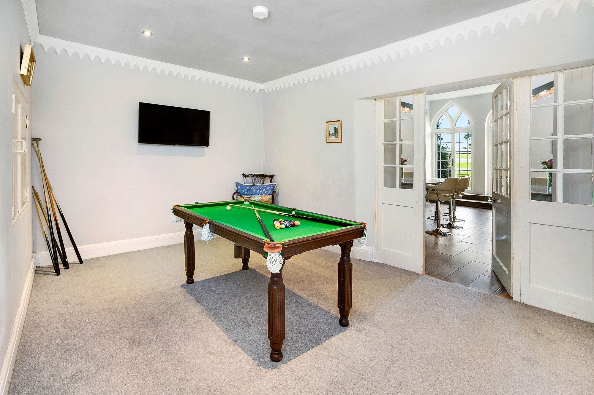 A room with a pool table, a television mounted on the wall, and a door leading to a dining area.