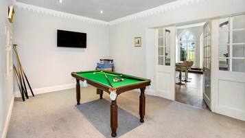 A room with a pool table, a television mounted on the wall, and a door leading to a dining area.