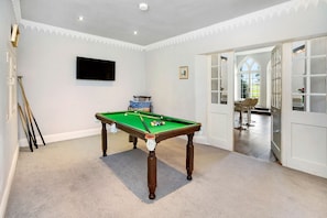 Una habitación con mesa de billar, televisor montado en la pared y puerta que da a un comedor.