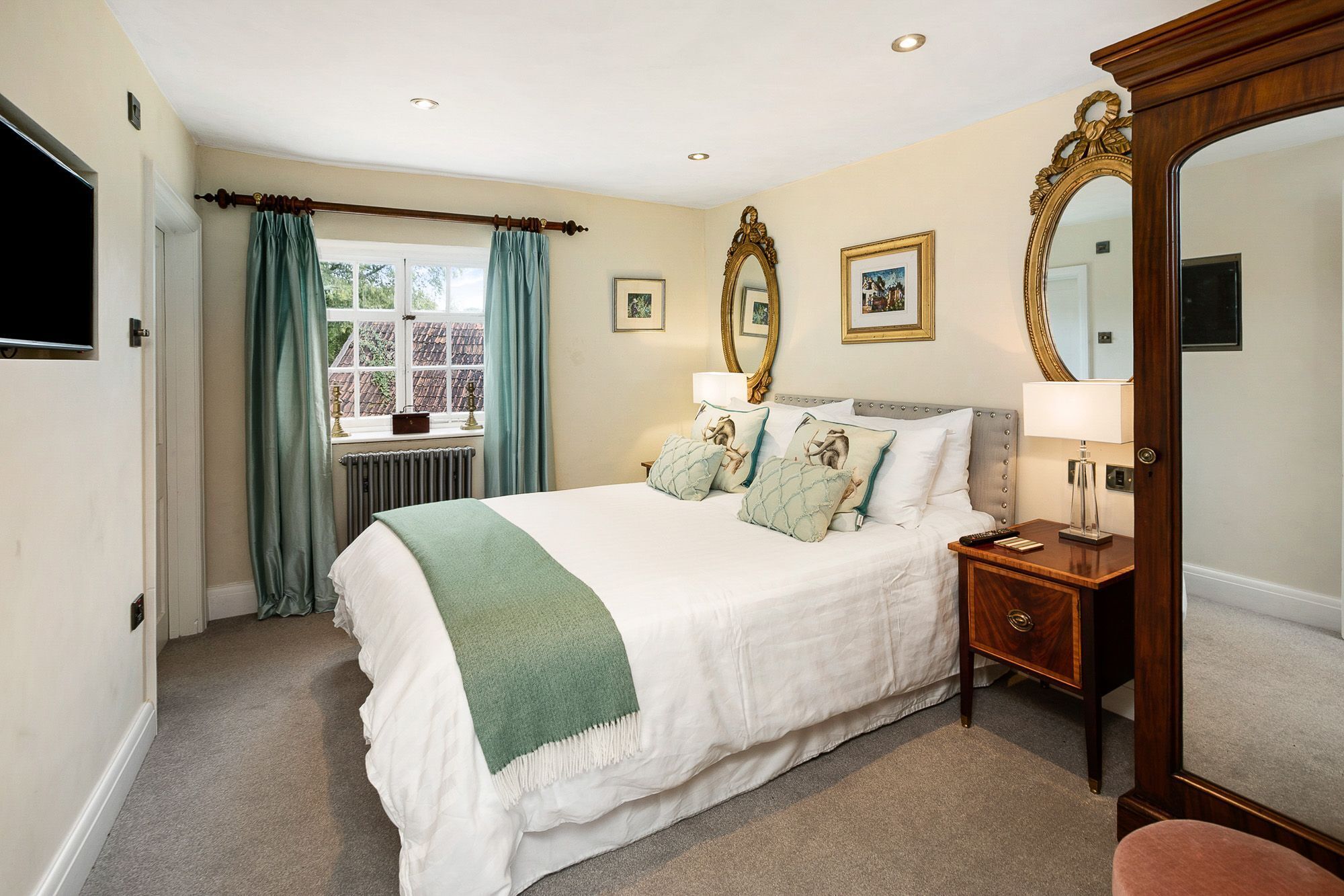 A hotel room with a bed, bedside tables, a mirror, and a window with curtains.