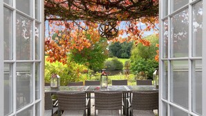 An open patio with a table and chairs, overlooking a garden with autumn foliage and a pond.
