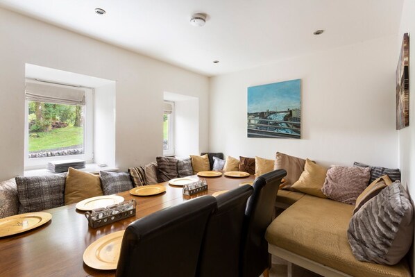 A dining area with a wooden table set for four, surrounded by a sofa and chairs.
