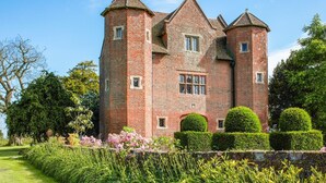 Un grand château en briques rouges, doté de nombreuses tours et agrémenté d’un jardin bien entretenu.