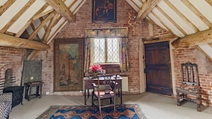 Une chambre mansardée au style rustique, avec des poutres apparentes, une grande fenêtre offrant une vue dégagée, un bureau avec une chaise et une porte traditionnelle.