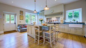 A spacious kitchen with a central island, white cabinetry, and a large window providing natural light. - Derwent Garden Estate (Bridekirk)