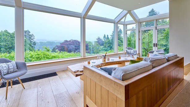 A modern room with a wooden bench and a chair, large windows offering a view of greenery and hills. - Derwent Garden Estate (Bridekirk)
