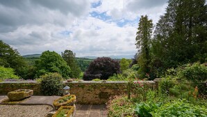 A garden with stone walls, various plants, and a view of distant hills. - Derwent Garden Estate (Bridekirk)