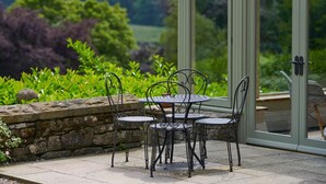 A patio with a table and chairs, a stone wall, and a glass door leading to a garden. - Derwent Garden Estate (Bridekirk)