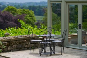 Un patio con una mesa y sillas, un muro de piedra y un ventanal de vidrio que da a un jardín.