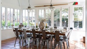 A dining area with a large table set for six, surrounded by metal chairs. There are two hanging pendant lights above the table, and a large vase with dried flowers in the center. - Meadow Manor - Seven Bedroom Villa, Sleeps 14 (Mundesley)