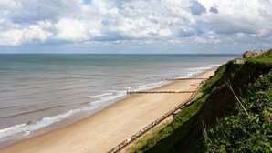 A beach with a wooden walkway along the shore, a grassy cliff, and a house in the background. - Meadow Manor - Seven Bedroom Villa, Sleeps 14 (Mundesley)