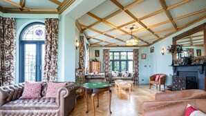 A spacious living room with a high ceiling, a fireplace, and a large window with curtains. - Culver Down Manor - Seven Bedroom Villa, Sleeps 16 (Shanklin)