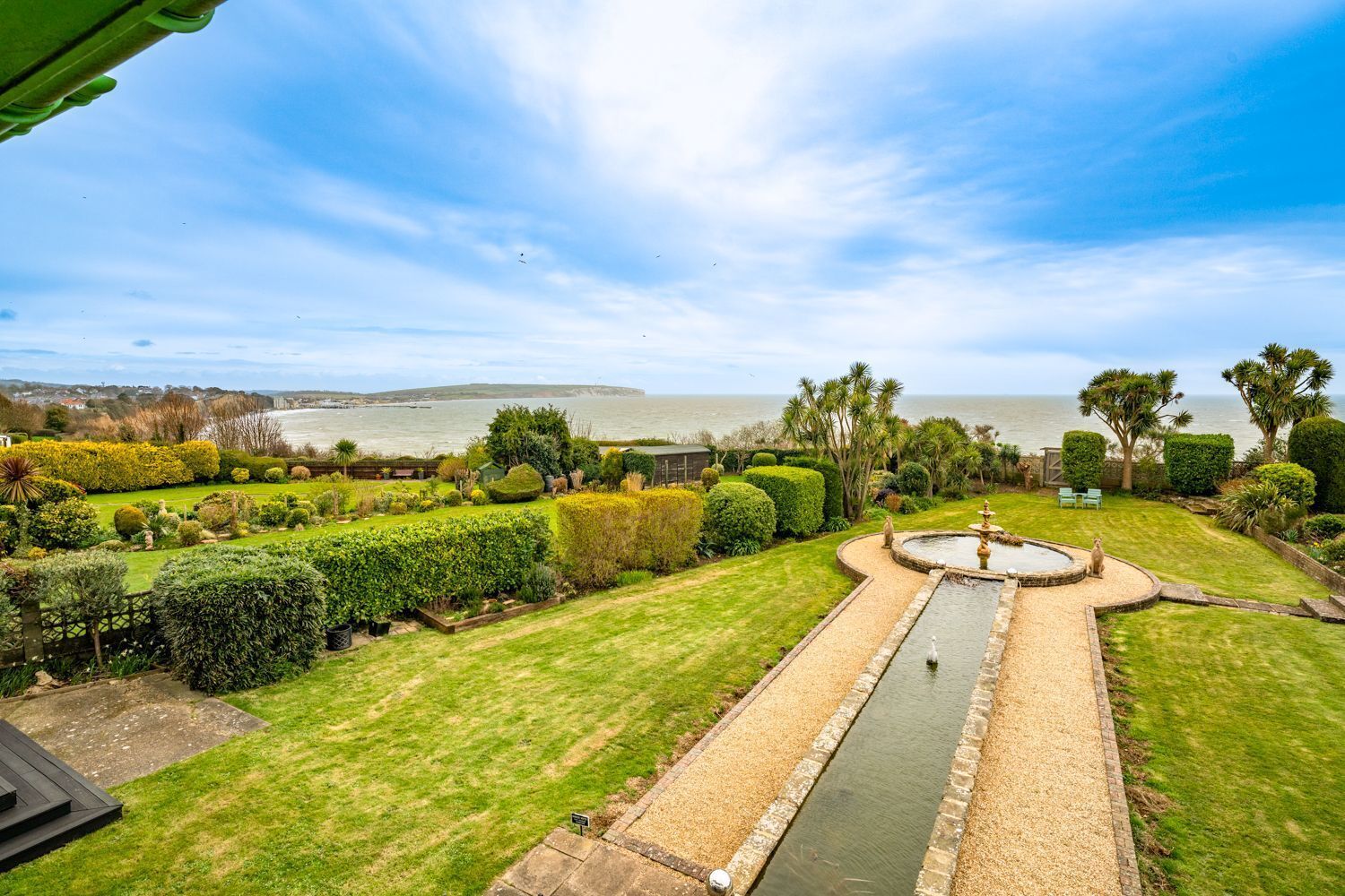 A well-maintained garden with a central water feature, surrounded by neatly trimmed hedges and a variety of plants.