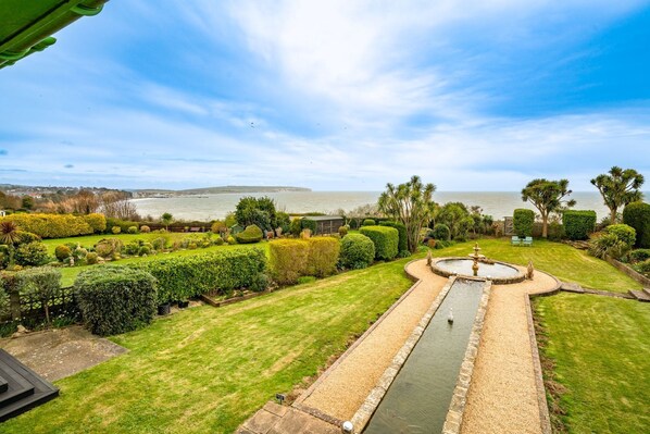 A well-maintained garden with a central water feature, surrounded by neatly trimmed hedges and a variety of plants.
