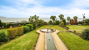 A well-maintained garden with a central water feature, neatly trimmed hedges, and a view of the sea. - Culver Down Manor - Seven Bedroom Villa, Sleeps 16 (Shanklin)