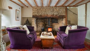 A cozy living room with a stone fireplace, two purple sofas, and a patterned rug.