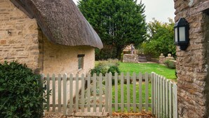 A stone cottage with a thatched roof, a picket fence, and a well-maintained garden.