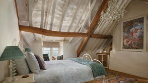 A bedroom with a sloped ceiling, a bed with a white and green bedspread, a wooden floor, and a painting on the wall.