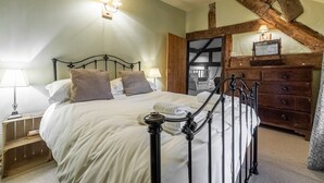 A bedroom with a bed, bedside lamps, a wooden dresser, and a rustic ceiling beam. - Tanat Valley Farmhouse (Hirnant)