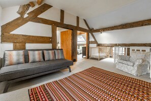 Un salon moderne avec des poutres apparentes, un canapé gris, des coussins à motifs et un tapis à motifs.