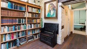 A room with wooden bookshelves filled with books, a black bench, and a painting on the wall. - Tanat Valley Farmhouse (Hirnant)