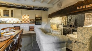 A kitchen with white cabinets, a dining table with chairs, and a built-in bench. There is a stone wall with a fireplace and a clock on the wall. - Tanat Valley Farmhouse (Hirnant)
