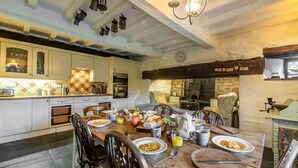 A rustic kitchen with a wooden dining table set for breakfast, featuring a stone fireplace and exposed wooden beams. - Tanat Valley Farmhouse (Hirnant)