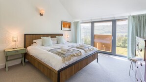 Un dormitorio con una cama grande, una mesita de noche, un tocador y vistas al exterior a través de una puerta corrediza de vidrio.