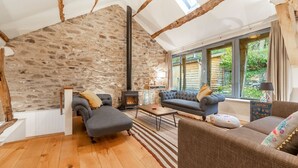 Una sala de estar acogedora con pared de piedra, vigas de madera, chimenea y asientos cómodos.