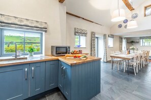 A modern kitchen with a large island, a dining area with a table and chairs, and a view of the countryside.