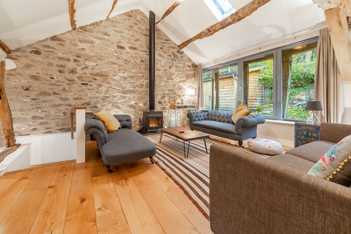 A cozy living room with a stone wall, wooden beams, a fireplace, and comfortable seating.