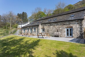 A stone building with a sloped roof, multiple windows, and a door. There are picnic tables outside.