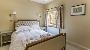 A neatly made bed with white linens, a wooden headboard, and a bedside table with a lamp. - Chevaliers Moat House (Upton Cressett)