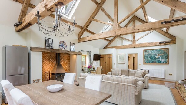 A spacious living area with a wooden dining table, white upholstered sofas, and a high ceiling with exposed beams. - Chevaliers Moat House (Upton Cressett)