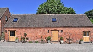 A brick building with two arched doorways and a central wooden door, surrounded by gravel and potted plants. - Chevaliers Moat House (Upton Cressett)
