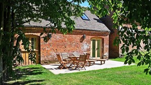 A brick building with a patio area, outdoor seating, and a tree providing shade. - Chevaliers Moat House (Upton Cressett)