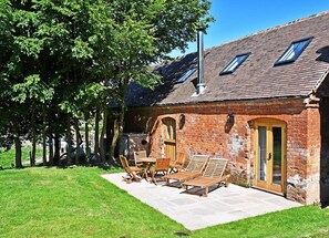 Un bâtiment en briques avec un toit en pente, une terrasse en bois dotée de chaises longues et une porte avec des panneaux de verre.