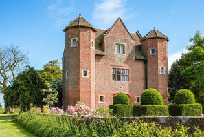 Un grand château en briques rouges, doté de nombreuses tours et agrémenté d’un jardin bien entretenu.