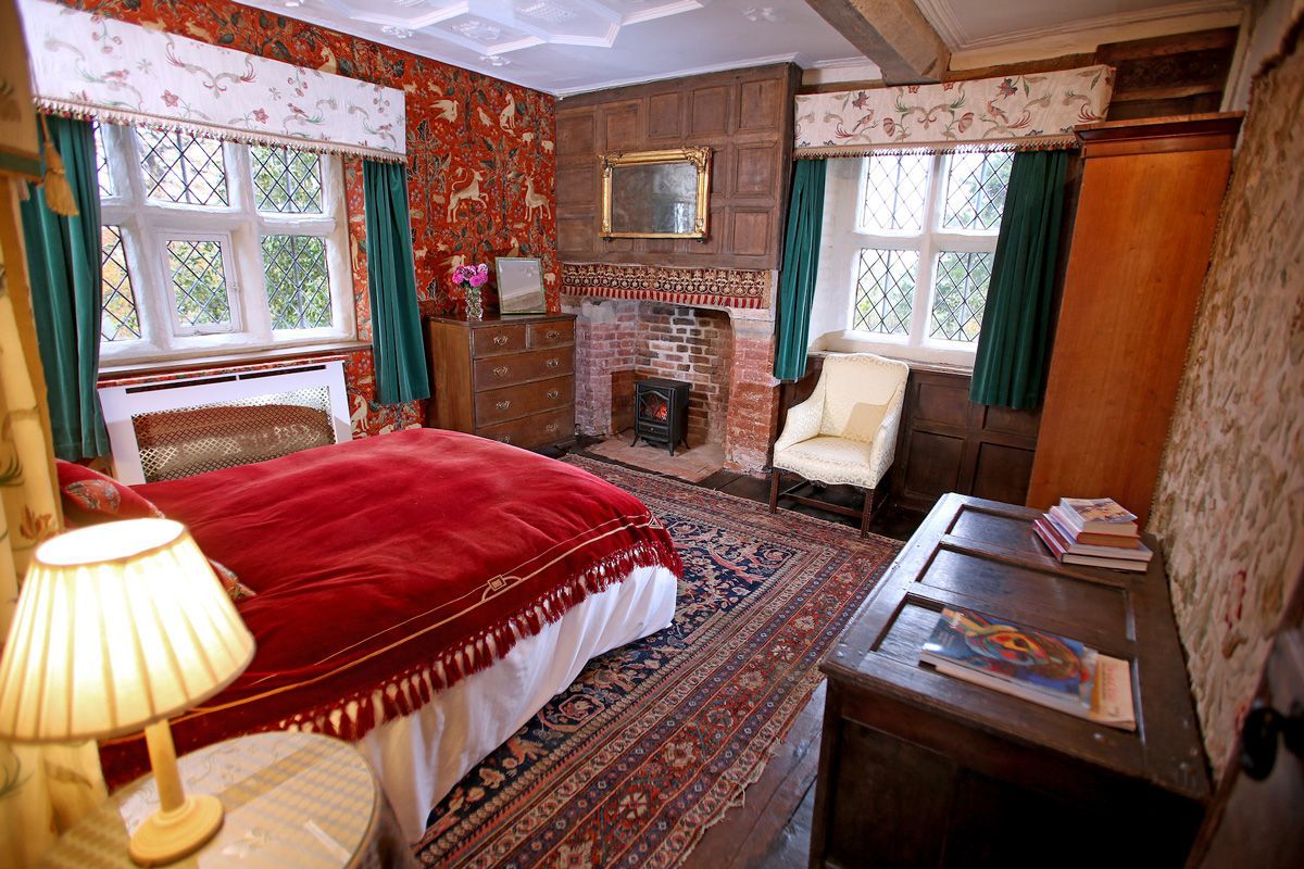 A traditional room with a bed, a fireplace, a wooden dresser, and a chair.