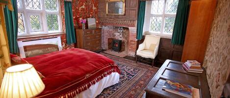 A traditional room with a bed, a fireplace, a wooden dresser, and a chair.
