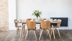 A dining area with a brick wall, wooden chairs, a round table, and hanging pendant lights.