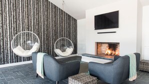 A modern living room with a fireplace, two grey sofas, a round hanging chair, and a patterned wallpaper.